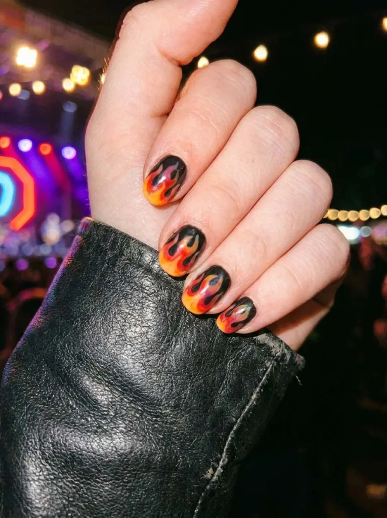 Hand raised at a concert with orange and red flame nail art under neon lights