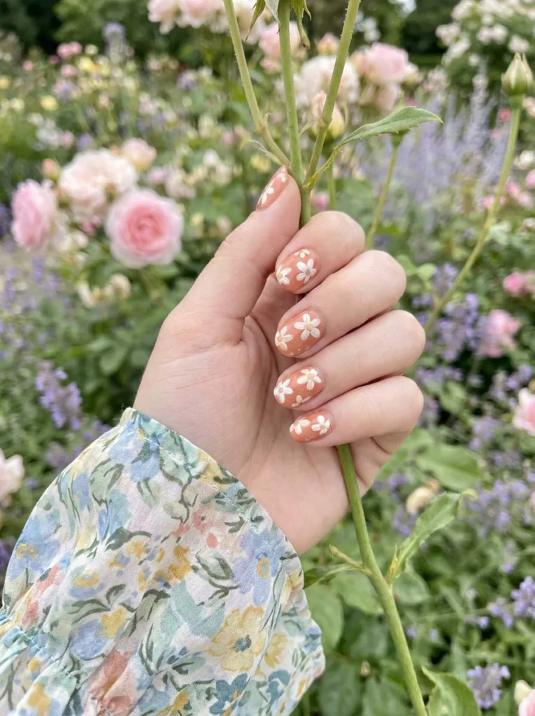 Hand with orange floral nail art touching a flower in a garden