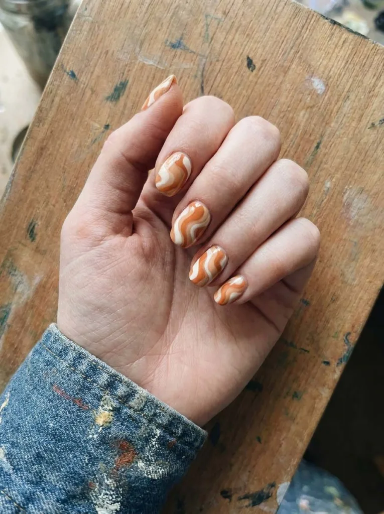 Hand with swirled orange and white marble nail art resting on a painter's palette