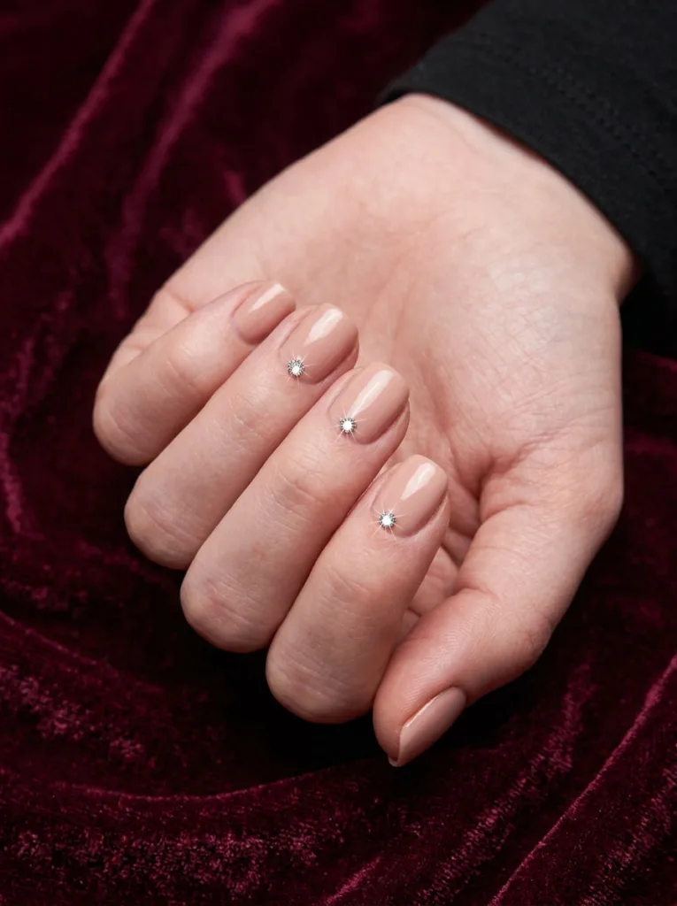 rhinestone accent nail art single crystal stone on nude blush fair skin nails against deep burgundy velvet