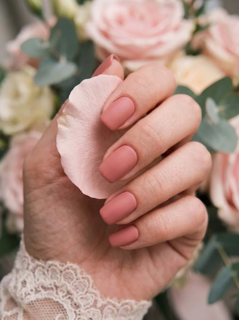 close-up of soft pink wedding nails beside a blush bridal bouquet