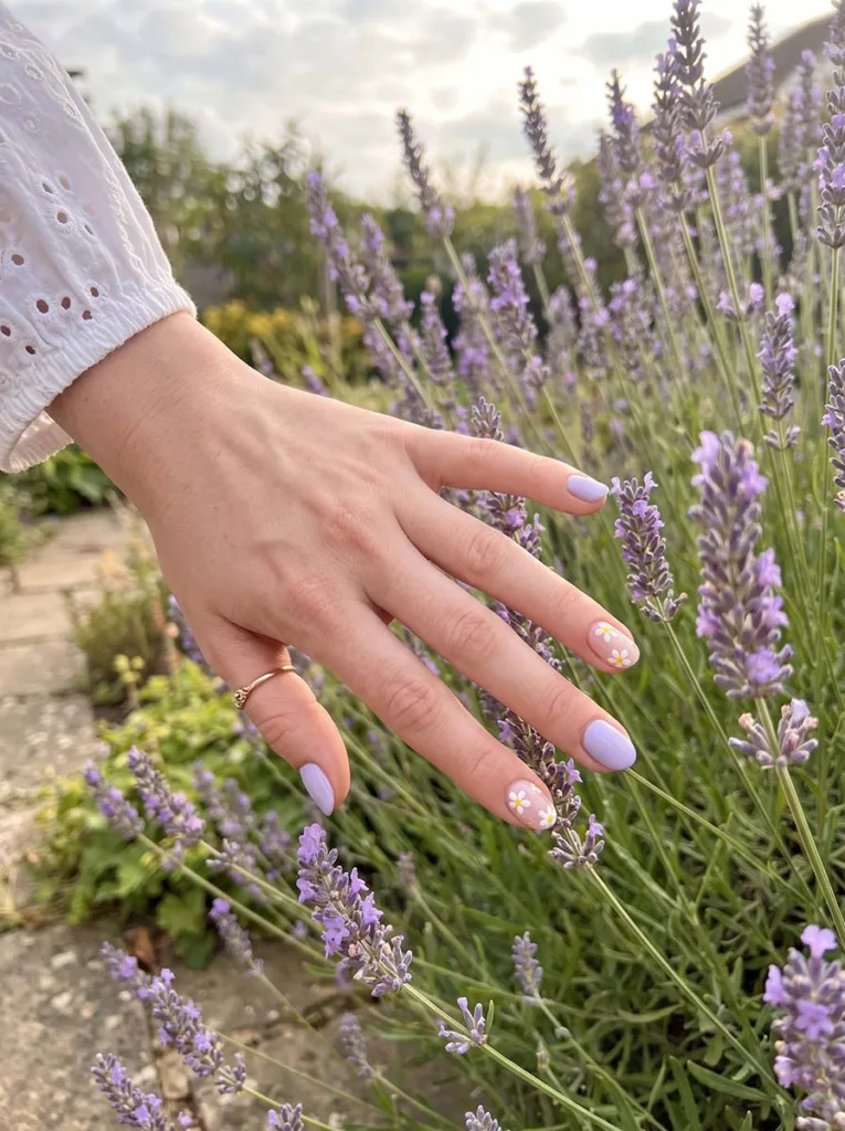 Fair-skinned hand with pastel lavender floral accent nails reaching toward real lavender stalks in a spring garden