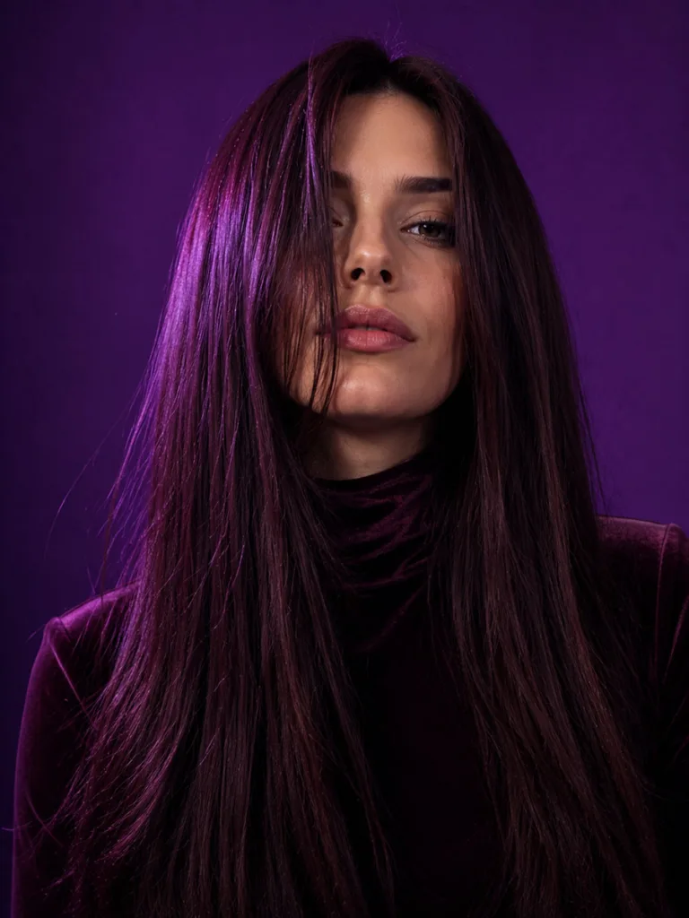 Dramatic aubergine brunette hair color against a vibrant violet-purple studio backdrop