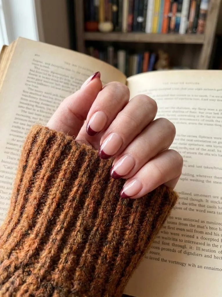 Hand with burgundy French tip nails resting on an open book