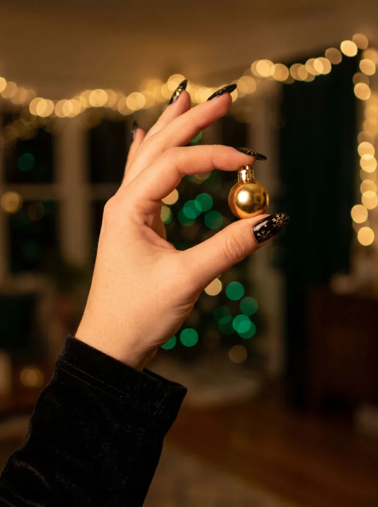 Fair-skinned hand in black velvet holding a gold ornament with black and gold snowflake christmas nails.