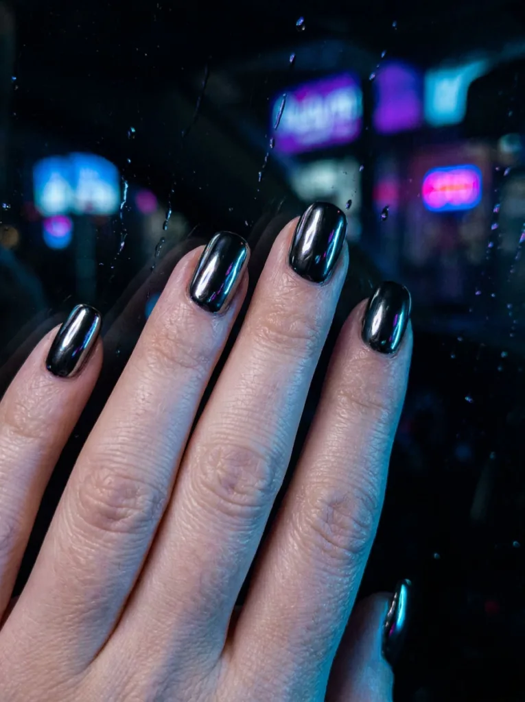Close-up of fingertips against glass, mirror-finish black chrome nails