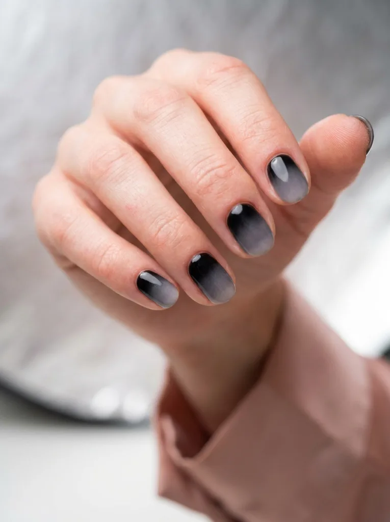 Close-up of fingertips showing a black-to-grey ombre manicure, nails