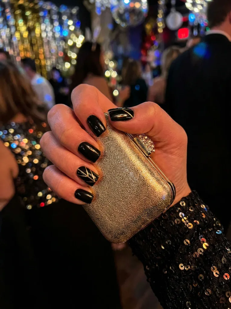 Fair-skinned hand with black and gold glam square winter nails holding a gold clutch purse