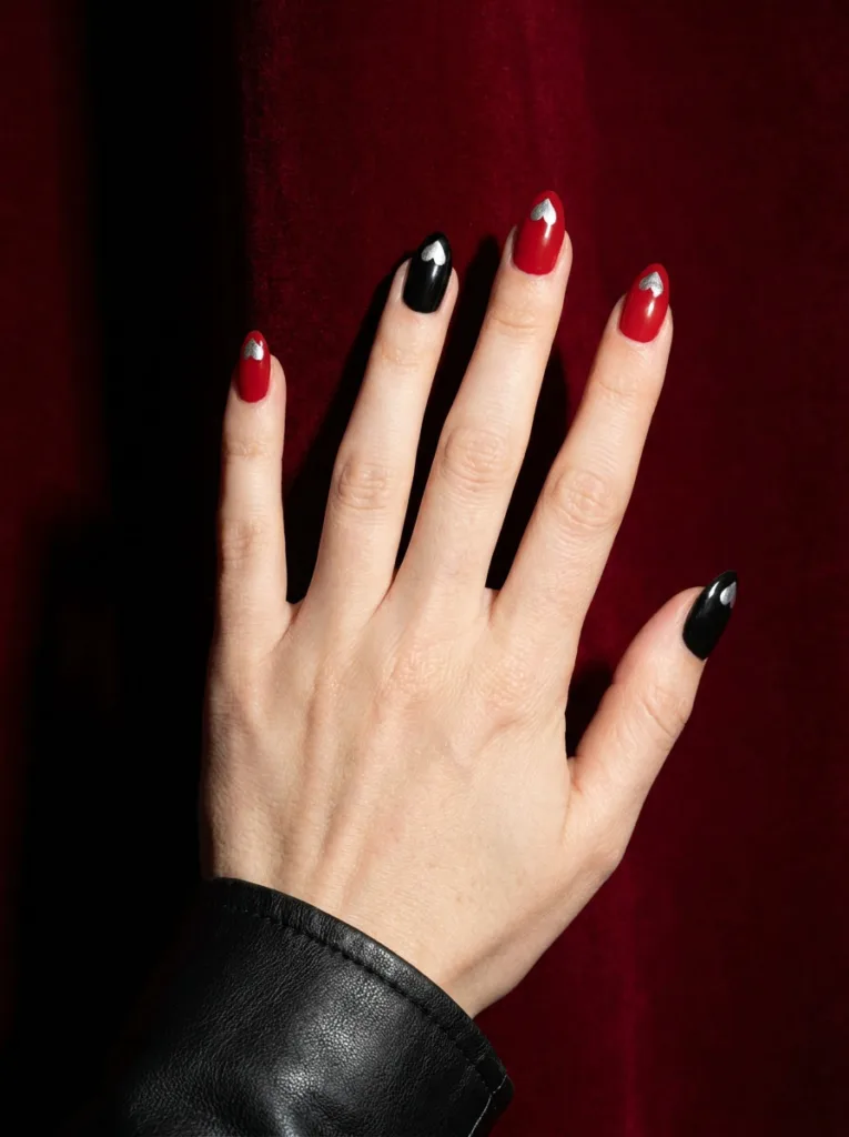 Fair-skinned hand with alternating black and red almond nails and silver heart accents