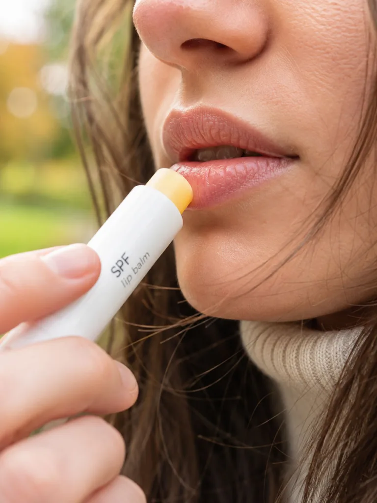 Woman in her 20s applying SPF lip balm to prevent early lip aging