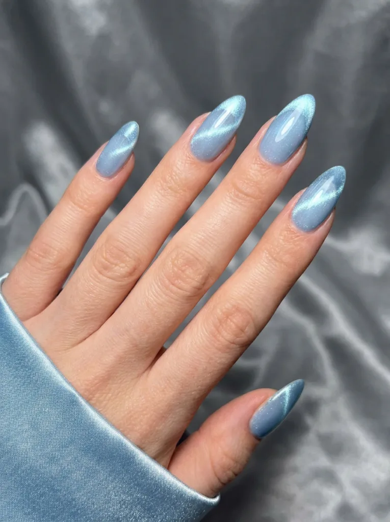 Hand with icy blue magnetic cat-eye French tip nails on almond-shaped nails