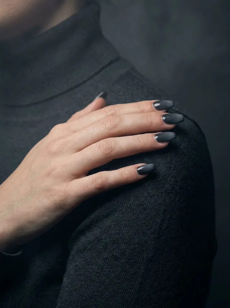 Fair-skinned hand resting on shoulder showing charcoal gradient ombre simple winter nails