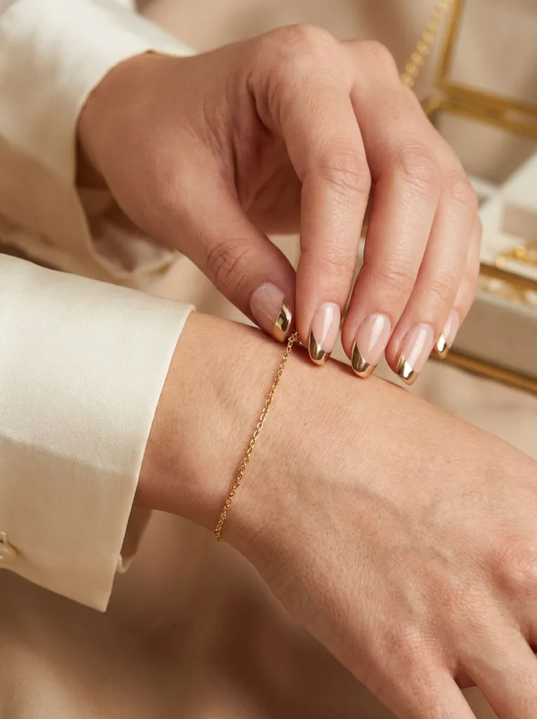 Hand with chrome gold French tip nails adjusting a gold bracelet