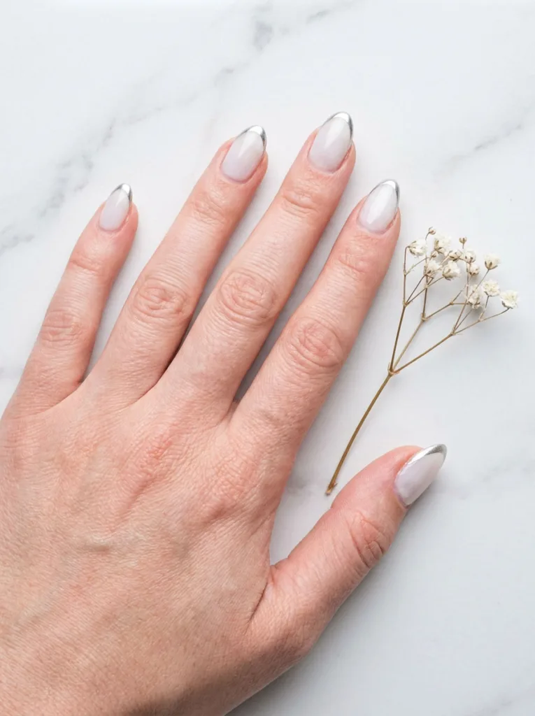 Thin metallic chrome outline traced along the smile line of a sheer white winter French manicure