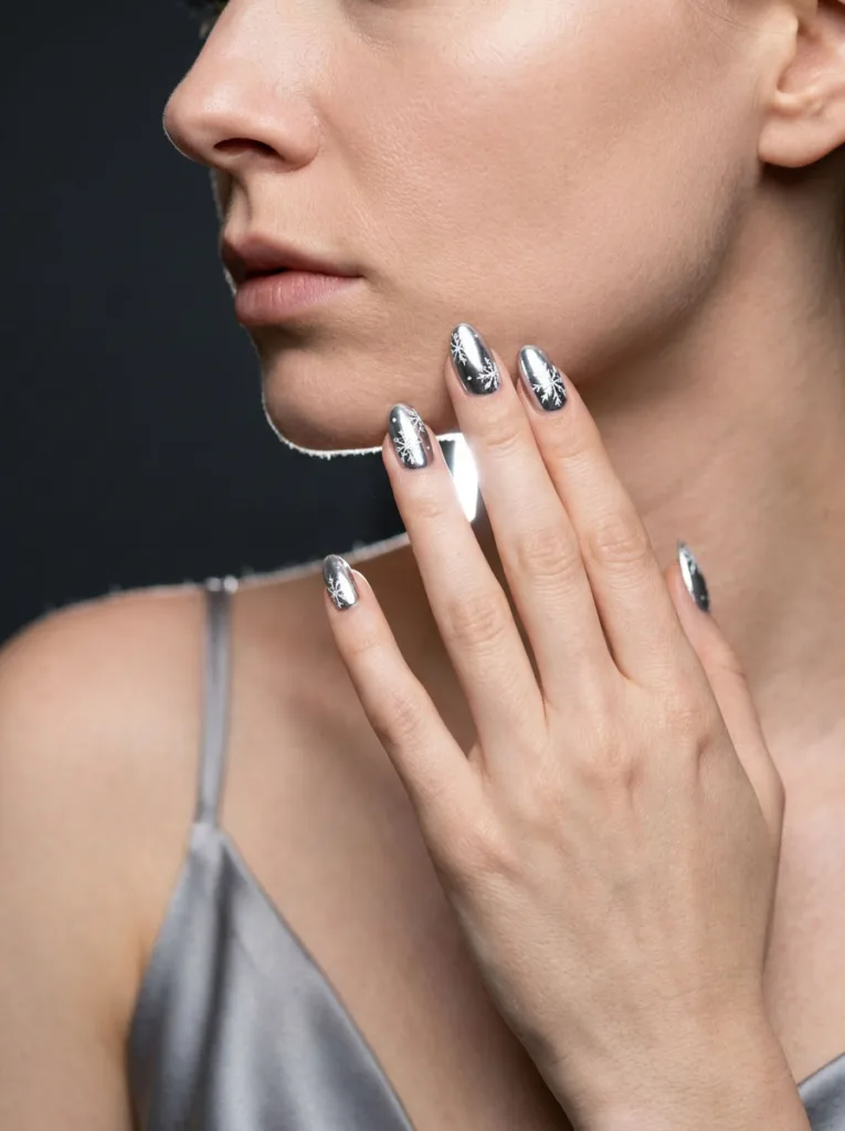 Fair-skinned model with chrome silver snowflake christmas nails raised beside her face.