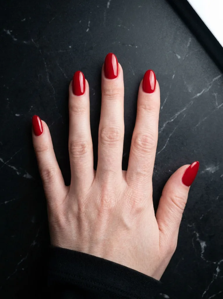Fair-skinned hand with classic red almond valentines day nails on black marble