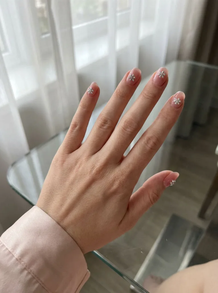 Fair-skinned hand on glass table showing clear jelly snowflake christmas nails with rhinestones.