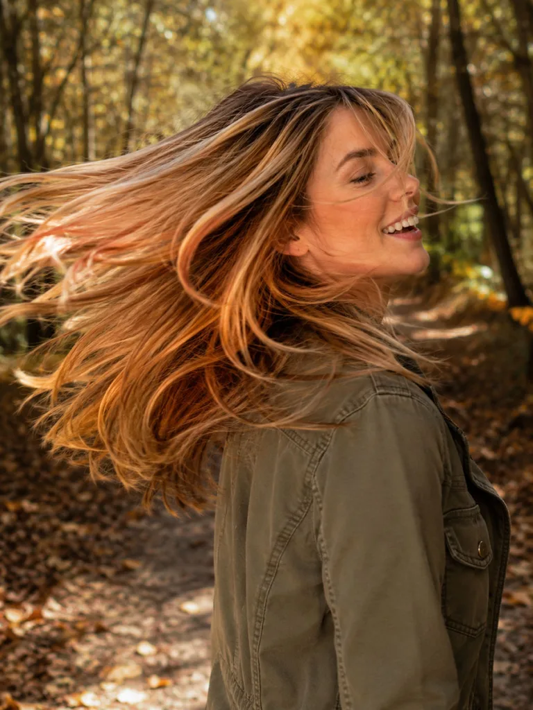 Woman flipping copper-kissed blonde fall hair color on a forest trail