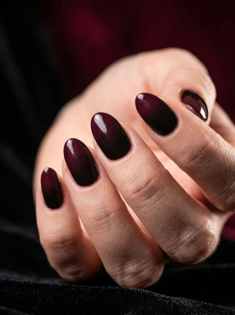 Hand with black-to-burgundy ombré nails against a velvet backdrop
