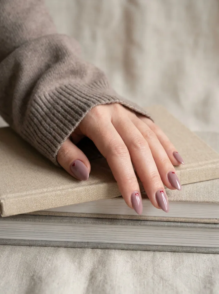 Fair-skinned hand with dusty mauve almond nails resting on a stack of books