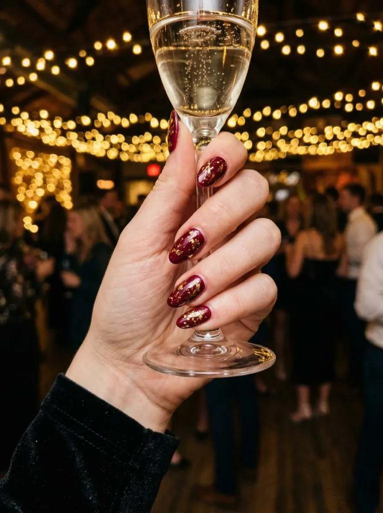 Hand with gold foil burgundy nails holding a champagne flute