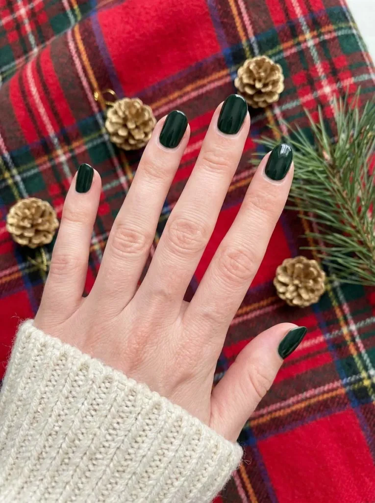 Fair-skinned hand with forest green simple winter nails resting on a red and green plaid blanket