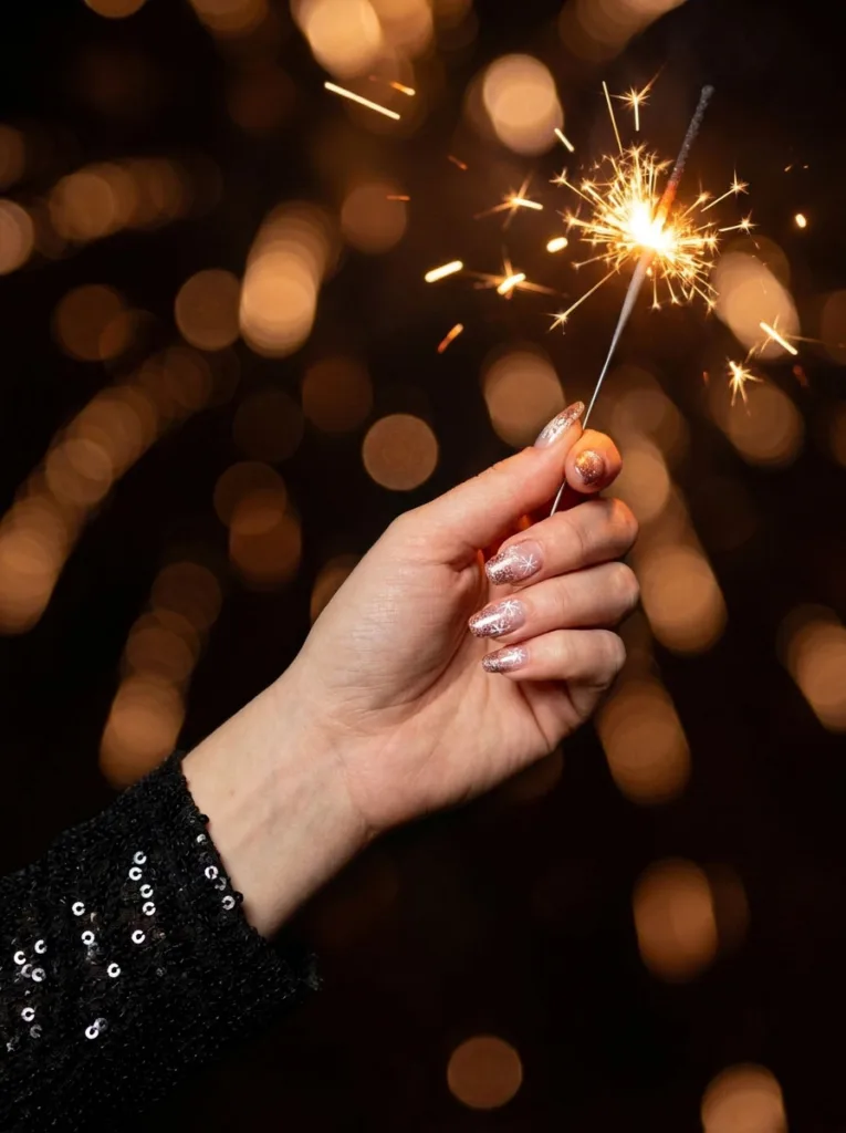 Fair-skinned hand holding a sparkler showing glitter gradient snowflake christmas nails.