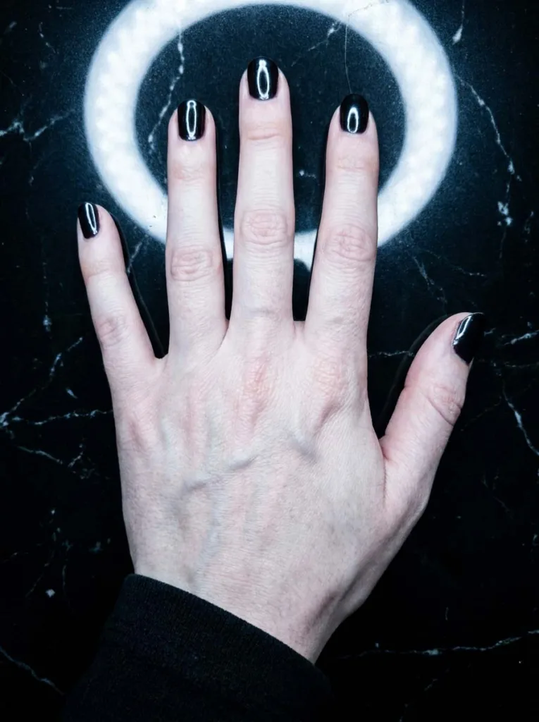 Glossy burgundy nail tips reflecting light on a black marble surface
