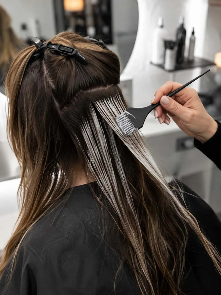 Colorist hand-painting brunette balayage lightener onto brown hair with a brush