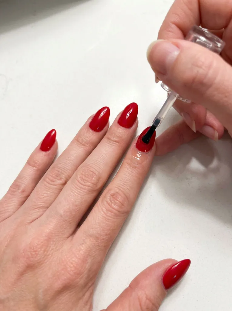 Applying top coat to a fair-skinned hand's almond shaped nail for longer wear