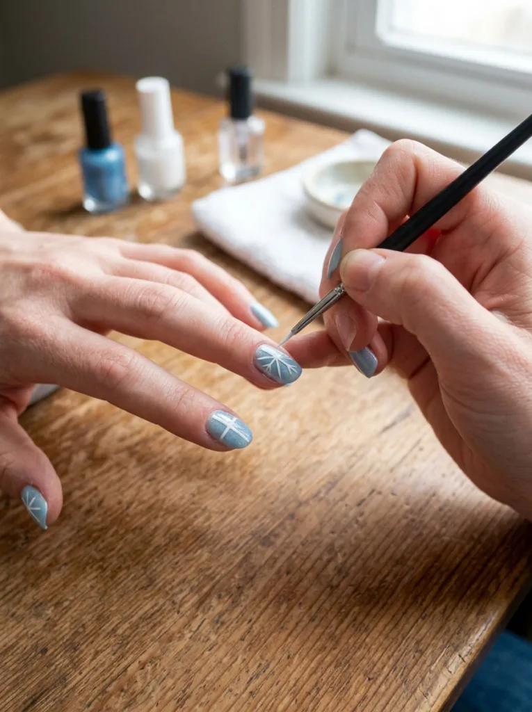 Fair-skinned hand painting a snowflake nail design step by step with a thin brush.