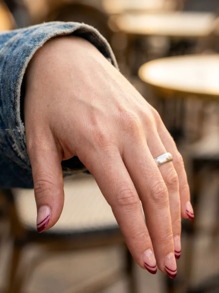 Hand with double outline burgundy French tip nails on a denim jacket sleeve
