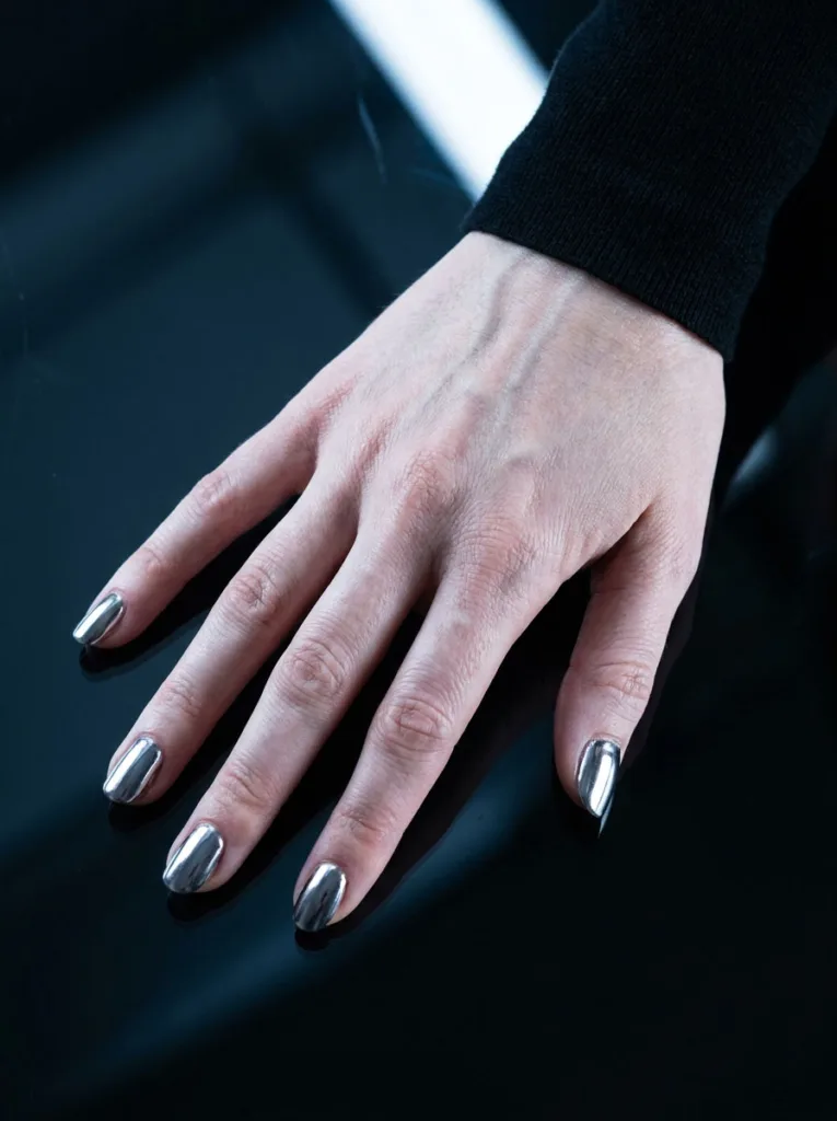 Hand with mirror-finish burgundy chrome nails over a reflective black surface