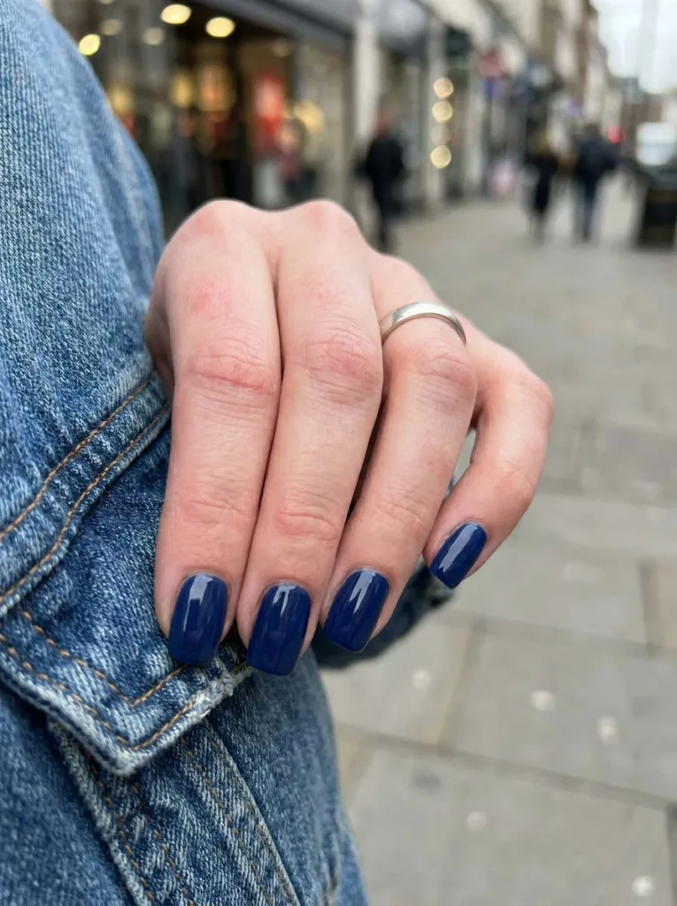 Fair-skinned hand tucked into a denim jacket pocket showing navy blue simple winter nails