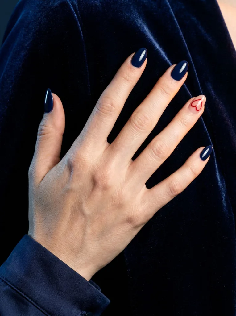 Fair-skinned hand with navy blue and red accent almond nails against navy velvet