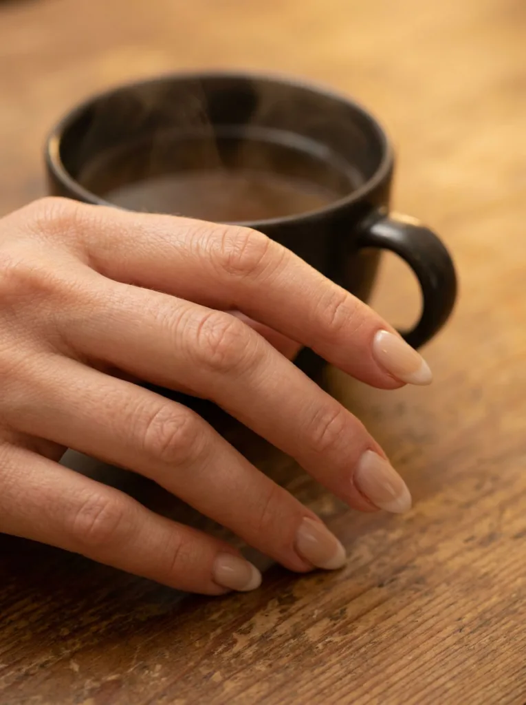 Beige base with a soft blurred smile line on winter French tip nails, hand resting near a warm mug of tea