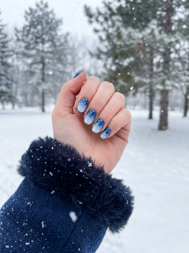 Fair-skinned hand cupped outdoors catching snow, showing ombre blue snowflake christmas nails.