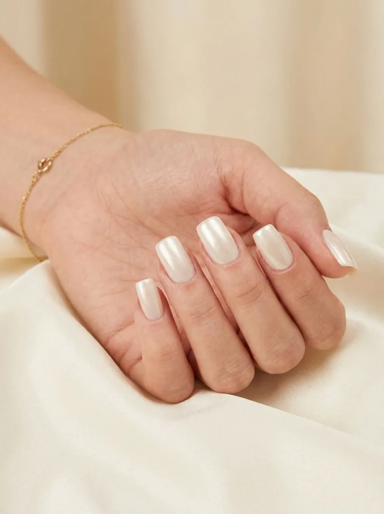 Pearl white birthday nails on a hand resting on silk fabric