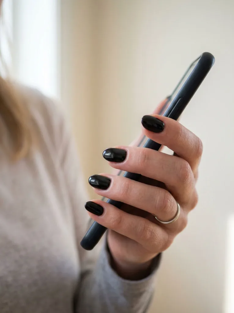 Close-up of a hand holding a phone, short oval-shaped black nails