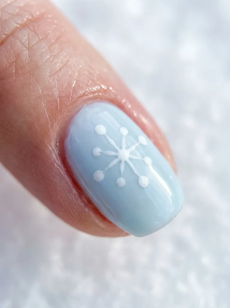 Fair-skinned hand with a single snowflake dot accent nail among soft blue simple winter nails