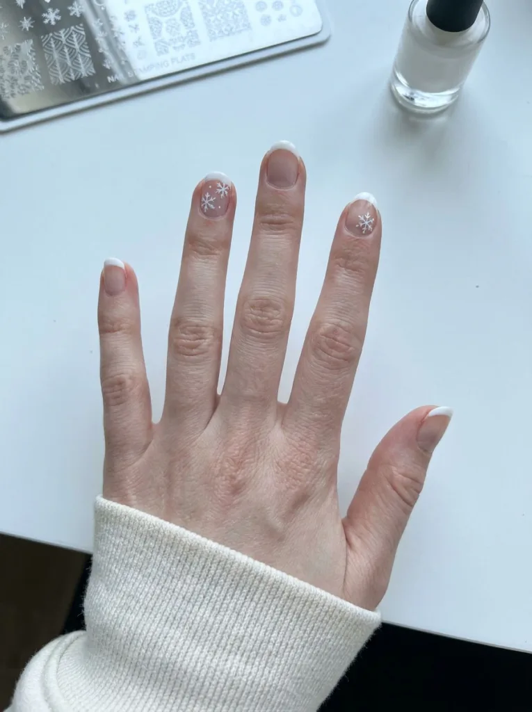 Close-up of hand with white French tips and hand-painted snowflake nail art