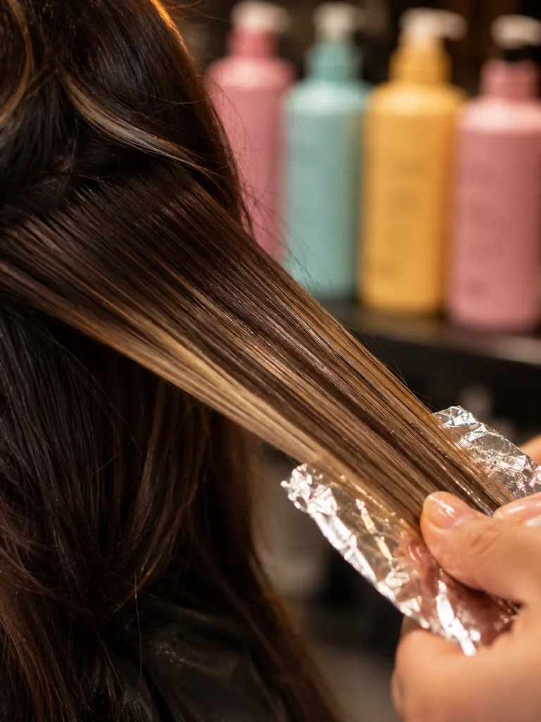 Close-up of a colorist testing a strand of brunette hair against vibrant pastel salon bottles