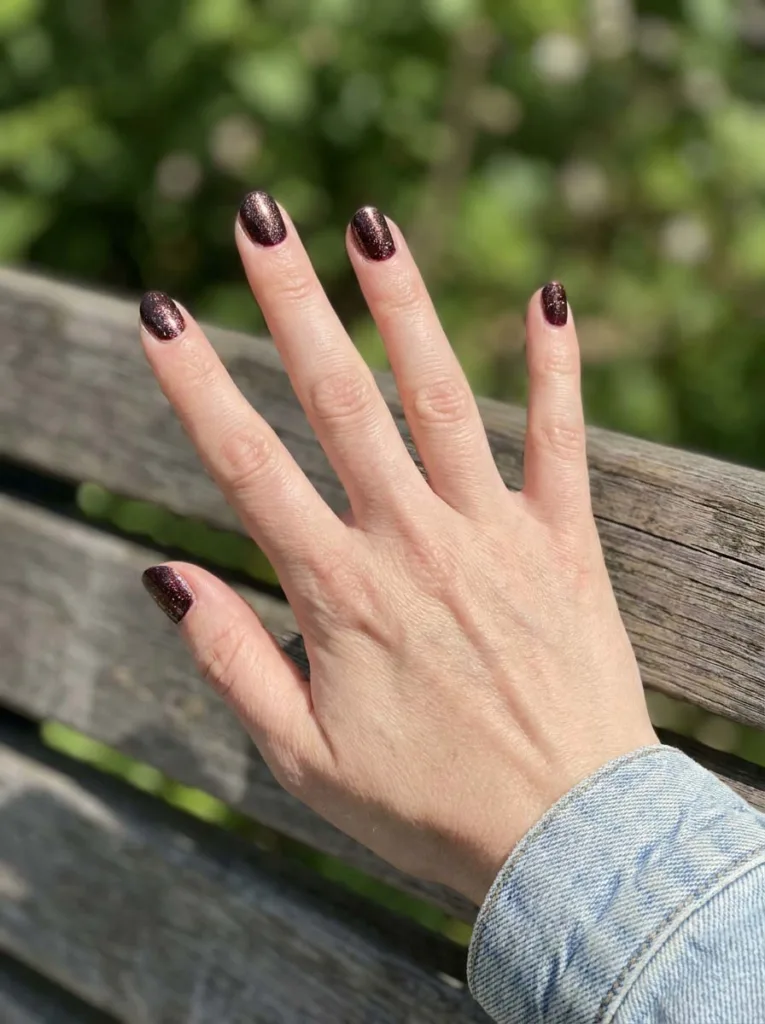 Hand with shimmer burgundy nails in outdoor sunlight
