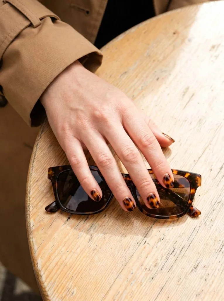 Hand with tortoiseshell burgundy nail art next to tortoiseshell sunglasses