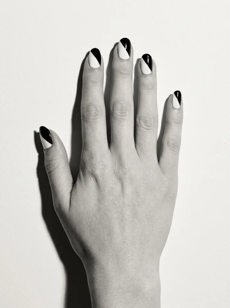 Close-up of a hand pressed flat against a wall, graphic two-tone black and white French tips