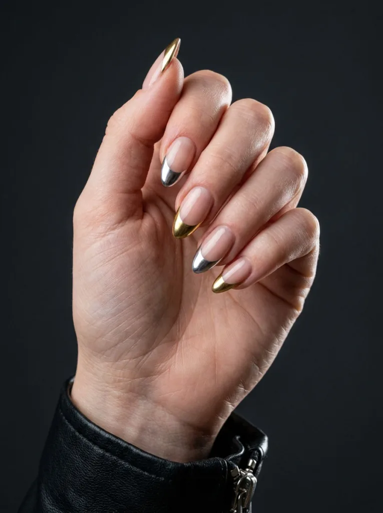 Alternating gold and silver chrome French tips on winter nails against a dark dramatic background