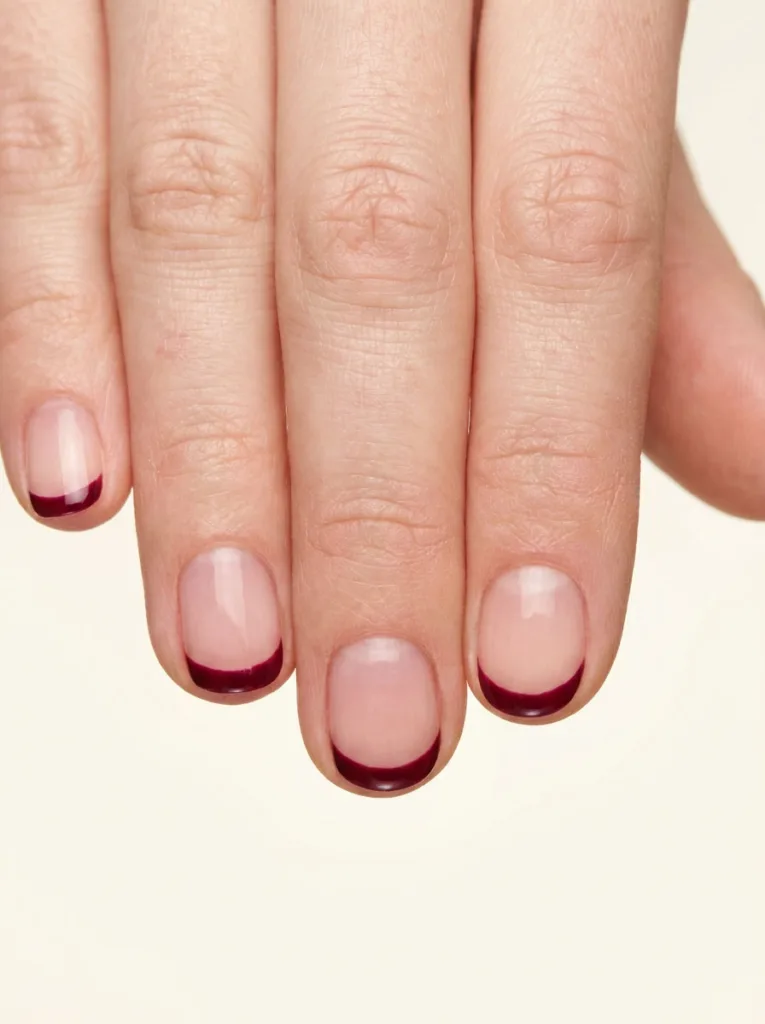 Close-up of micro French burgundy nail tips against a neutral background