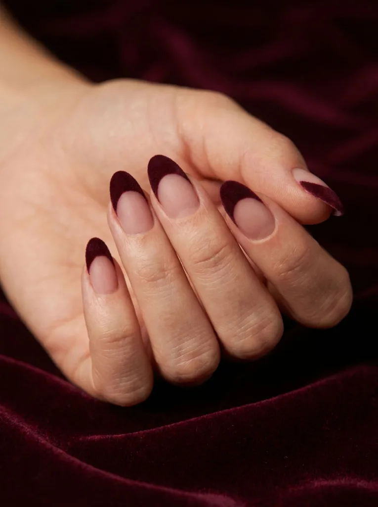 Deep burgundy matte velvet-finish French tips resting against a draped velvet fabric backdrop