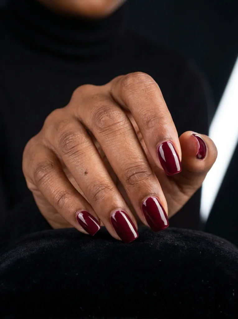 Deep skinned hand with glossy burgundy nail polish resting against black velvet fabric.