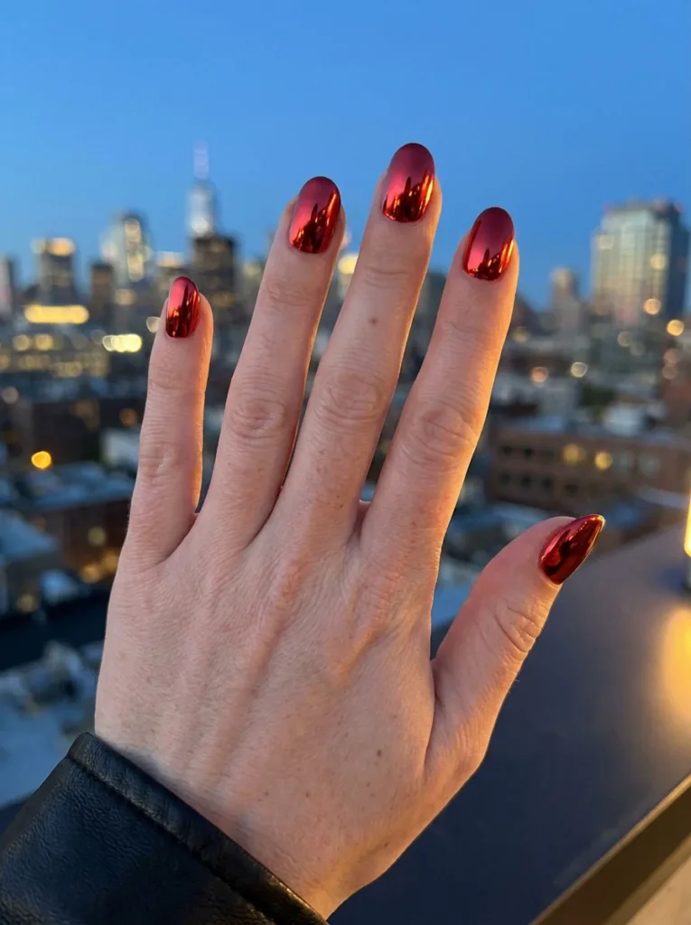 Close-up of red chrome nails reflecting city lights at dusk.